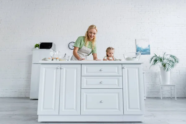 Vista de ángulo bajo de la madre y la hija cocinar en la mesa de la cocina blanca - foto de stock