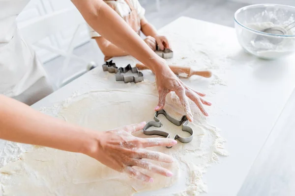 Visão cortada de mulher cortando massa com cortador de biscoitos perto da filha na cozinha — Fotografia de Stock