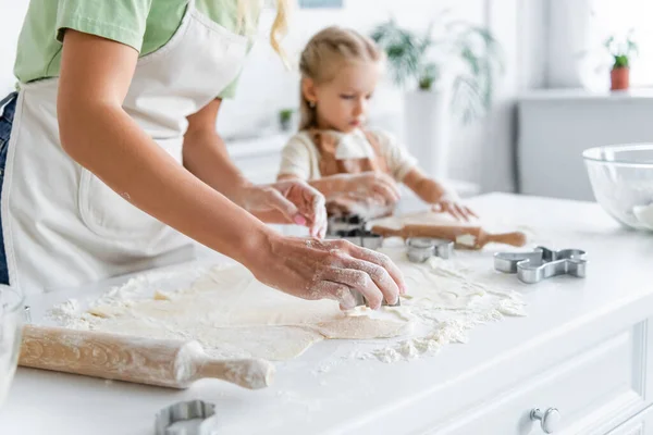 Femme coupe la pâte avec coupe-biscuits près enfant flou dans la cuisine — Photo de stock