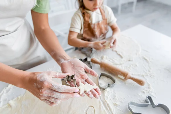 Vista cortada de mulher segurando biscoito cru em forma de abeto perto menina borrada na cozinha — Fotografia de Stock