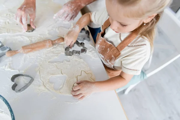 Blick von oben auf das Kind, das Teig mit Ausstecher in der Nähe der Mutter in der Küche schneidet — Stockfoto