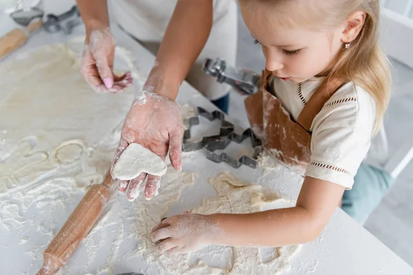 Vista ad alto angolo di donna che mostra biscotti crudi a forma di cuore a figlia in cucina — Foto stock