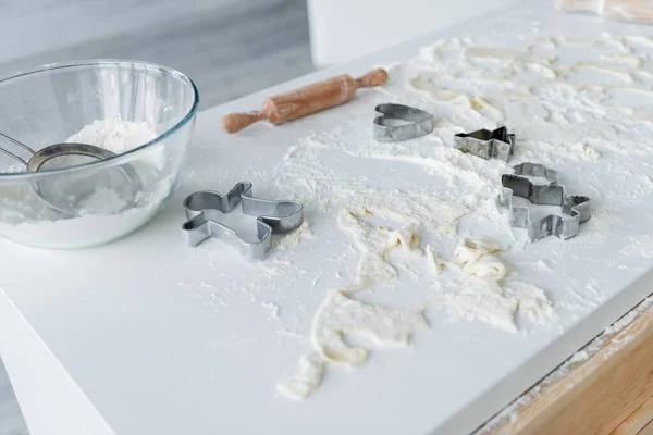Tazón de vidrio, tamiz, cortadores de galletas y rodillo en la mesa blanca con harina dispersa - foto de stock