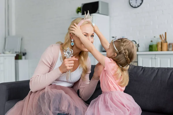 Girl putting toy crown on head of mother while playing at home — Stock Photo
