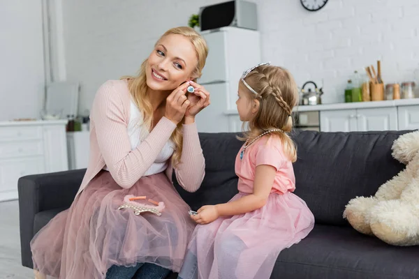 Smiling woman putting on earring near daughter in fairy costume — Stock Photo
