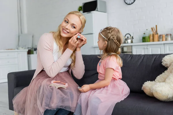 Sonriente mujer poniendo en pendiente cerca de hija en traje de hadas - foto de stock