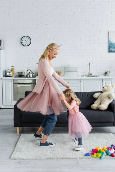 Cheerful woman and child in fairy costumes holding hands while dancing at home — Stock Photo