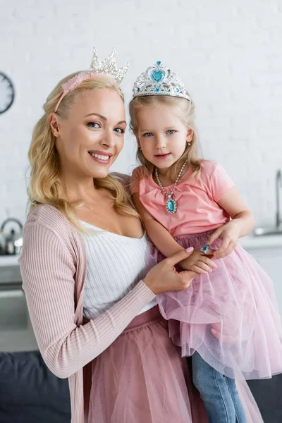 Joyful woman and girl in toy crowns looking at camera at home — Stock Photo