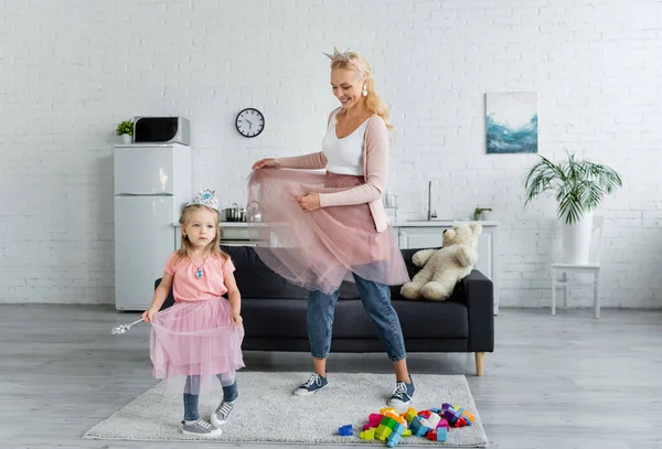 Fröhliche Frau und Kind in Prinzessinnen-Kostümen, die in der Küche tanzen — Stockfoto