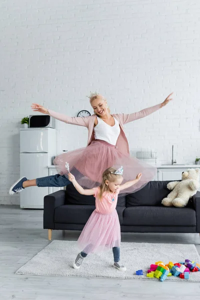 Збуджена жінка з дочкою танцює вдома в костюмах принцес — стокове фото