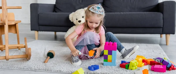 Enfant en costume de princesse jouant avec baguette magique et blocs de construction colorés sur le sol, bannière — Photo de stock