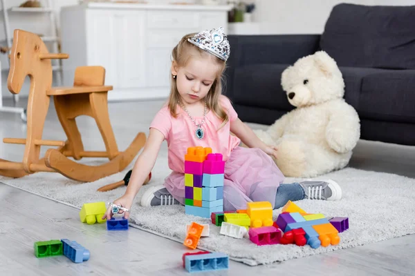 Child in fairy costume playing with colorful cubes on floor near blurred teddy bear — Stock Photo