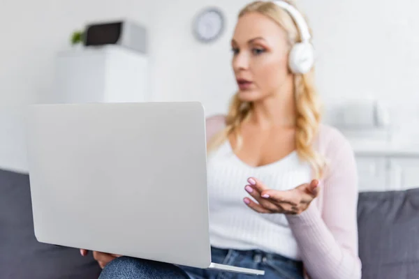 Blurred woman in headphones pointing with hand at computer during video call — Stock Photo