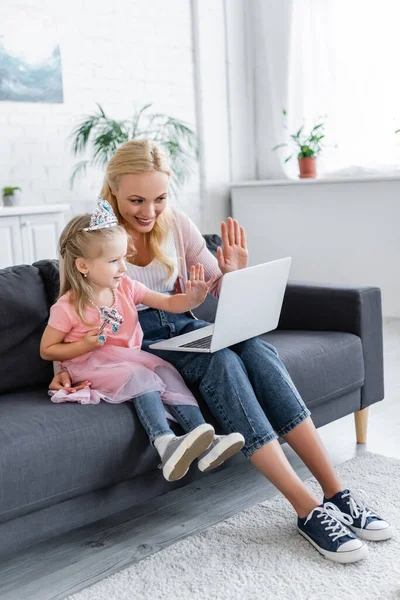 Mulher alegre e menina em brinquedo coroa acenando as mãos durante chamada de vídeo no laptop — Fotografia de Stock