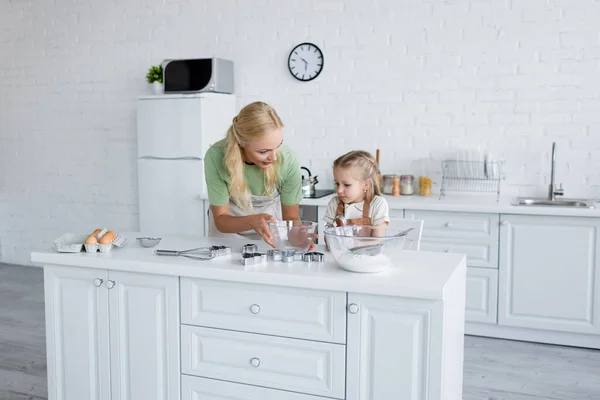 Mother holding bowl near daughter and kitchen table with ingredients — Stock Photo