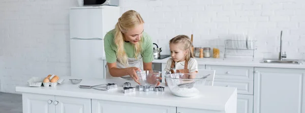Woman showing bowl to daughter while cooking together in kitchen, banner — Stock Photo