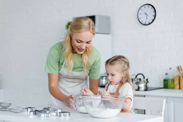 Kleines Mädchen sieben Mehl in Schüssel, während es mit Mama in der Küche kocht — Stockfoto