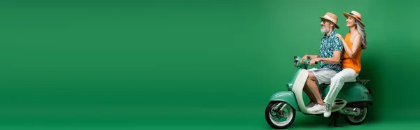 Alegre interracial e meia idade casal em sol chapéus equitação ciclomotor no verde, banner — Fotografia de Stock
