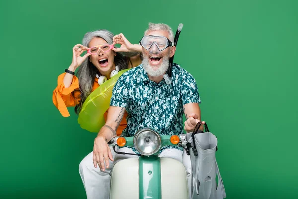 Многонациональная и возбужденная пара средних лет в очках верхом на мопеде изолированы на зеленый — стоковое фото