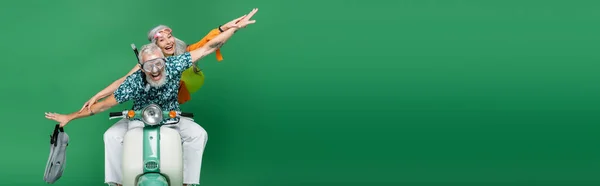Pareja multiétnica y alegre de mediana edad con las manos extendidas a caballo moto en verde, bandera - foto de stock