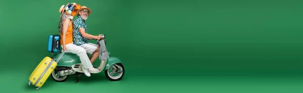 Mature asian woman in sun hat covering face with passports near husband holding flippers while riding moped on green, banner — Stock Photo