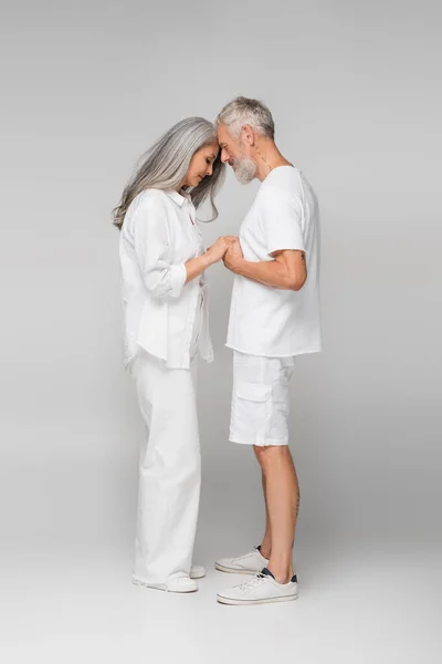 Comprimento total de casal interracial e maduro de mãos dadas em cinza — Fotografia de Stock