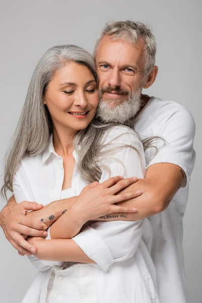 Happy and interracial mature couple hugging isolated on grey — Stock Photo