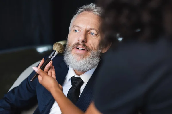 Blurred african american makeup artist applying face powder on businessman in interview studio — Stock Photo