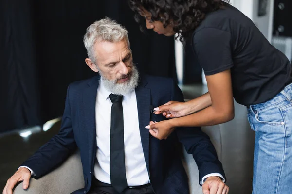 Curly african american assistant adjusting microphone on suit of businessman in interview studio — Stock Photo