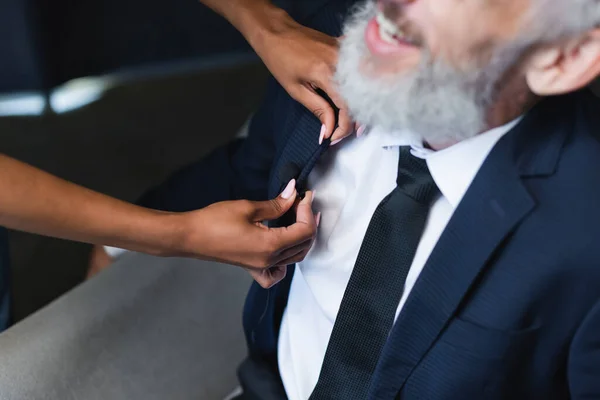 Cropped view of african american assistant adjusting microphone on suit of smiling businessman in interview studio — Stock Photo
