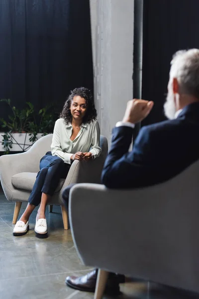 Lockiger afrikanisch-amerikanischer Journalist blickt während einer Talkshow auf unscharfen Geschäftsmann — Stockfoto