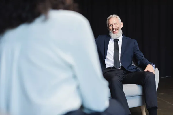 Empresário alegre em terno olhando para jornalista turvo durante a entrevista — Fotografia de Stock