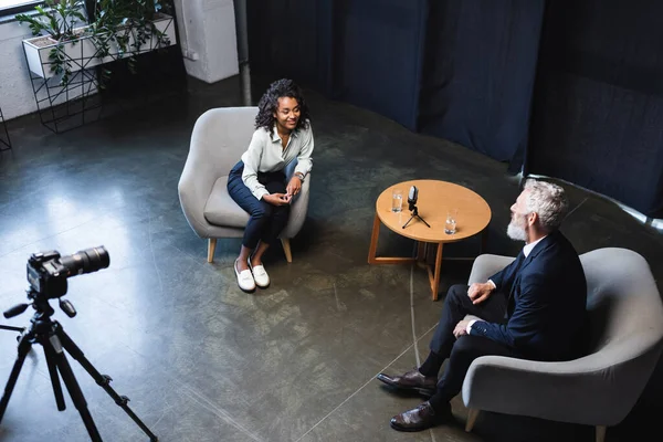 Blick aus der Vogelperspektive auf einen glücklichen afrikanisch-amerikanischen Journalisten im Gespräch mit einem Gast im Interview-Studio — Stockfoto