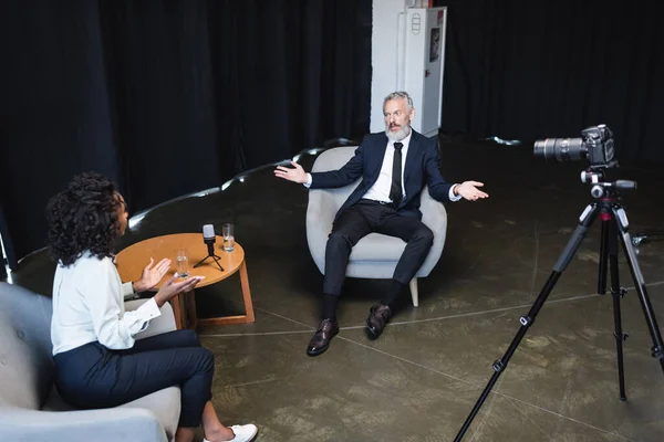 Vista de alto ángulo del hombre de negocios en traje gesto durante la entrevista con periodista afroamericano - foto de stock