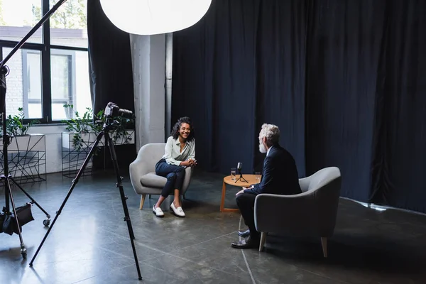 Alegre jornalista afro-americano conversando com convidado em estúdio de entrevista — Fotografia de Stock