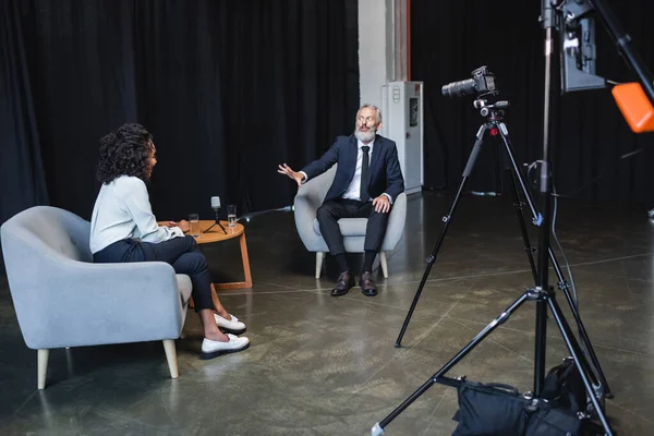 Empresario gesto mientras habla con rizado afroamericano periodista durante la entrevista - foto de stock