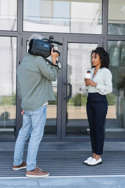 Full length of african american journalist doing reportage near cameraman outside — Stock Photo