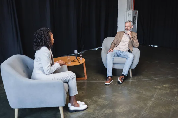 Curly african american journalist in suit talking with businessman sitting in armchair during interview — Stock Photo