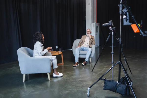 Африканский американский журналист беседует с улыбающимся бизнесменом, сидящим в кресле во время интервью — стоковое фото