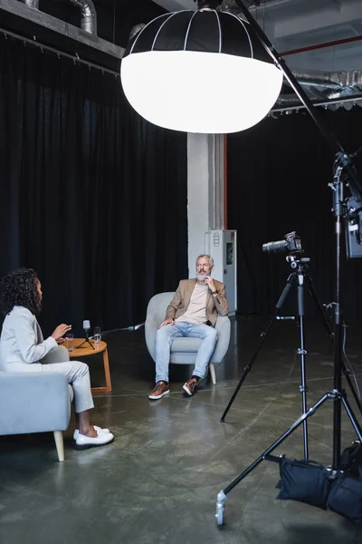 Giornalista afroamericano che parla con un uomo d'affari seduto sulla poltrona grigia durante l'intervista — Foto stock