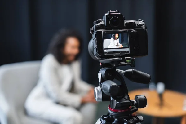 Câmera digital no tripé com jornalista afro-americano sentado em poltrona na tela — Fotografia de Stock