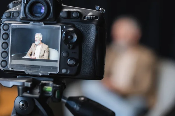 Modern digital camera with businessman sitting in armchair on screen — Stock Photo