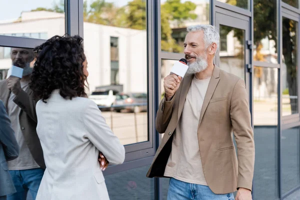 Reporter barbuto con microfono parlare vicino afro americano donna d'affari — Foto stock