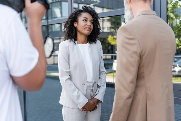 Reporter interviewt afrikanisch-amerikanische Geschäftsfrau in der Nähe verschwommener Kameramann mit Videokamera — Stockfoto