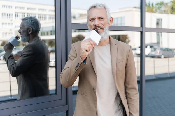 Bearded journalist in blazer holding microphone and making reportage near building — Stock Photo