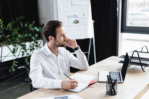 Nachdenklicher behinderter Geschäftsmann schaut weg, während er im Büro mit dem Smartphone spricht — Stockfoto