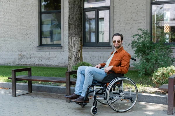 Jovem deficiente homem em cadeira de rodas sorrindo para a câmera na rua urbana — Fotografia de Stock