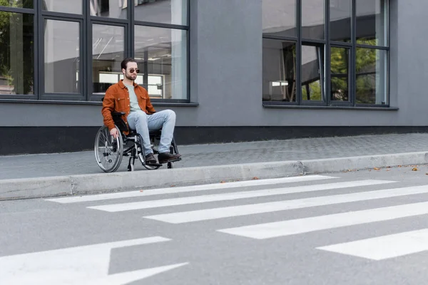 Young handicapped man sitting in wheelchair near border and crosswalk — Stock Photo