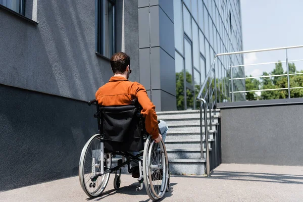 Vista trasera del hombre discapacitado en silla de ruedas cerca del edificio con escaleras al aire libre - foto de stock