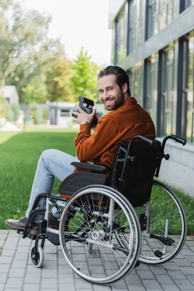 Glücklicher behinderter Mann im Rollstuhl lächelt in die Kamera, während er eine Oldtimer-Kamera hält — Stockfoto